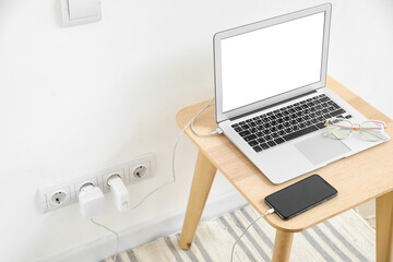 Table with charging laptop and mobile phone near light wall