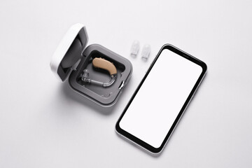 Box with hearing aid and mobile phone on white background