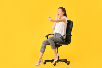 Shocked young woman with imaginary steering wheel sitting in chair on color background