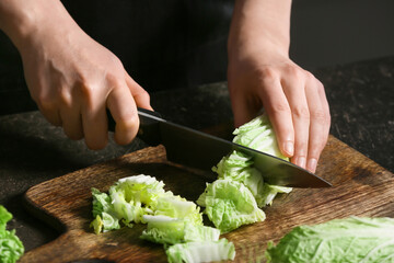 Woman cutting fresh chinese cabbage on table, closeup