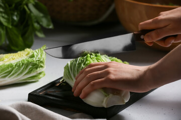 Woman cutting fresh chinese cabbage on table, closeup