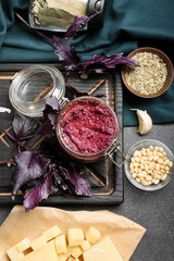 Composition with jar of tasty pesto sauce and ingredients on dark background