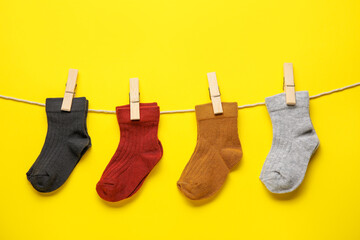 Different baby socks hanging on rope against color background