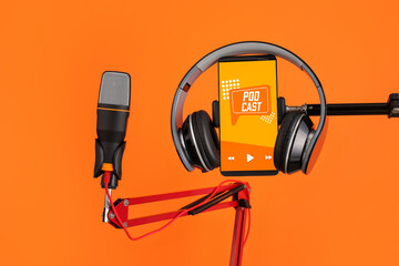 Modern microphone with headphones and mobile phone with with podcast playlist on screen against...