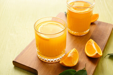 Board with glasses of tasty orange juice on color background, closeup