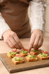 Woman decorating tasty sandwiches with tomato and guacamole at table, closeup