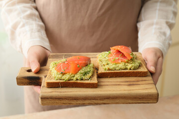 Woman holding board with tasty sandwiches on light background, closeup