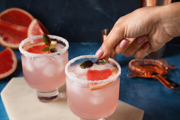 Woman decorating grapefruit margarita on color background, closeup