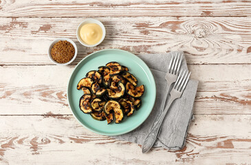 Plate of tasty grilled zucchini and bowls with sauce on light wooden background
