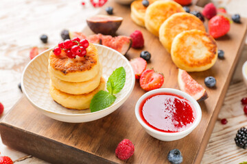 Board with cottage cheese pancakes, berries and jam on table, closeup