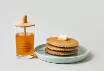 Plate of tasty pancakes with honey and butter on light background