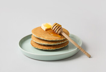 Plate of tasty pancakes with honey and butter on light background
