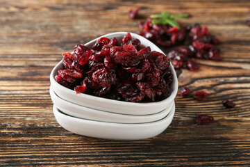 Bowl with tasty dried cranberries on wooden background, closeup