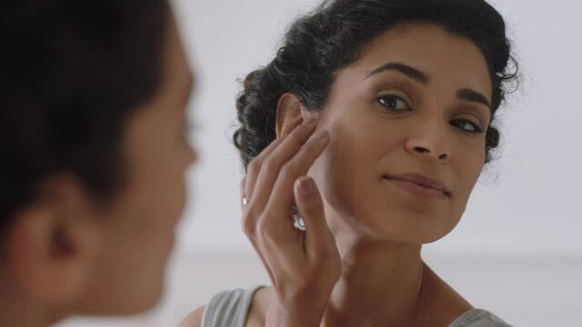 portrait beautiful young woman looking in mirror at perfect healthy skin touching face with hands enjoying smooth natural complexion with anti aging skincare getting ready at home beauty concept
