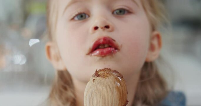 happy little girl licking spoon tasting delicious chocolate pudding enjoying homemade treats in kitchen 4k