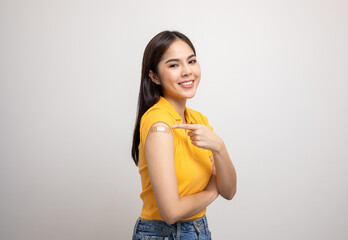 Vaccination. Young beautiful asian woman in yellow shirt getting a vaccine protection the coronavirus. Smiling happy female showing arm with bandage after receiving vaccination. - obrazy, fototapety, plakaty