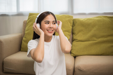 Relaxing time on sofa. Beautiful young asian woman sitting near sofa she choose music take a rest and listening song with headphone. Lifestyle in living room at house in the morning.