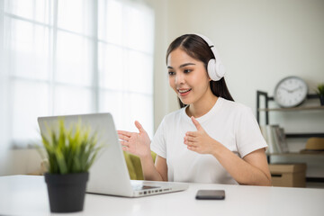 Young asian woman in headphone using laptop chatting video conference online sitting in living room...
