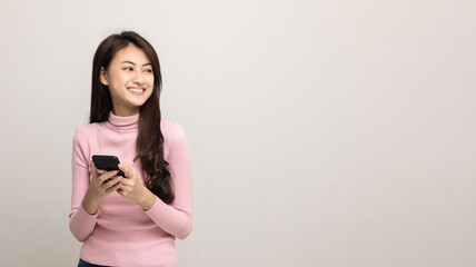 Pretty young asian woman using smartphone standing on isolated white background feeling happy looking blank space. Shopping online payment with mobile phone. Excited female holding cellphone.