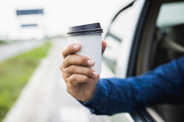 Young man drinking a cup of hot coffee while driving car to travel. Hands holding steering wheel. Take a break for a refreshing coffee before your trip.