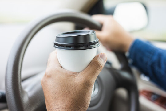 Young man drinking a cup of hot coffee while driving car to travel. Hands holding steering wheel.