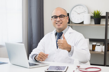 Young asian man doctor works from home working online looking and camera talking with patient Explain about taking medications to treat illnesses.