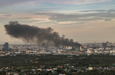 Naklejka premium Bangkok, Thailand - 19 Aug, 2021 : Plume of smoke clouds from Burnt industrial or office building on fire at some area in the city. Fire disaster accident, Selective focus.