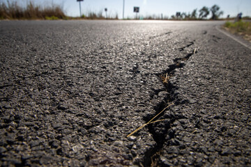 Close up of asphalt road surface crack with rural landscape in a background. 