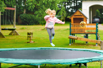 Little preschool girl jumping on trampoline. Happy funny toddler child having fun with outdoor...