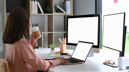 Asian businesswoman drinking coffee and working wit multiple devices in office.