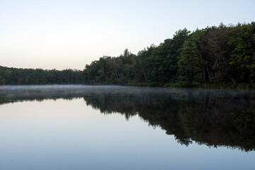 reflection of a forest by the lake with morning mist