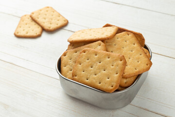 Cracker cookies in a stainless steel bowl on white wooden table background.