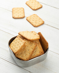 Cracker cookies in a stainless steel bowl on white wooden table background.