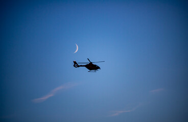 A rescue helicopter flies under the crescent moon early in the evening on its landing approach to a hospital