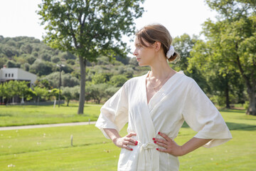 Portrait of young woman wearing linen kimono dress in the green country side enviroment