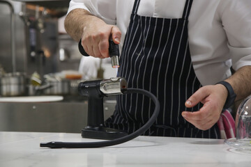Chef holding smoking gun in kitchen. Food equipment for innovative culinary technologie.