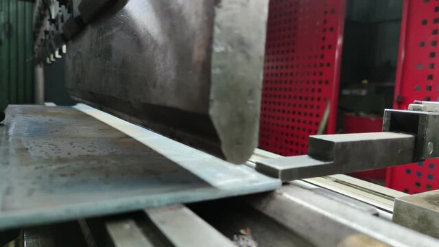 Bending a thick sheet of metal on a bending machine, close-up. The bending machine operator bends a sheet metal product. A worker works at a metalworking plant.