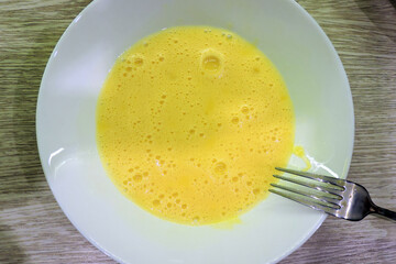 A close-up of foamy whisked eggs with a fork, whisked eggs in a white plate