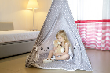 Cute toddler girl sitting in wigwam with her teddy bear in bedroom © triocean