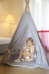 Cute toddler girl sitting in wigwam with her teddy bear in bedroom © triocean