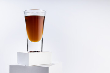 Old golden cognac in shot glass on top of stack of white square podiums, luxury alcohol drink in modern minimal geometric style, soft light space.