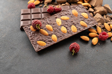 Cooking chocolate bars with almonds, raspberries, handmade sweets. Composition of bars and pieces of dark almond chocolate, raspberries on a black background, top view. Pastry craft on the table