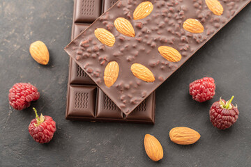 chocolate bars with almonds, raspberries, handmade sweets. Composition of bars and pieces of dark almond chocolate, raspberries on a black background, top view. Pastry craft on the table