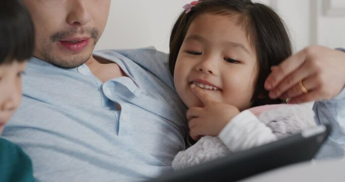 happy asian family using tablet computer at home mother and father with children watching entertainment playing game on touchscreen device learning having fun relaxing in bed 4k footage 