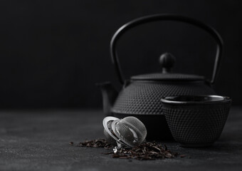 Black loose tea with strainer infuser and iron japanese teapot and cup on dark.