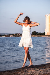 A young woman is standing on the beach. Photo of a beautiful tanned blonde in a white lace dress at...