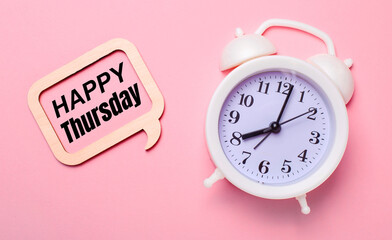 On a delicate pink background, a white alarm clock and a wooden frame with the text HAPPY THURSDAY