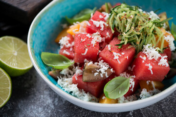 Close-up of salad with watermelon cubes, tomatoes, grated bryndza cheese and cucumber served in a turquoise bowl, studio shot