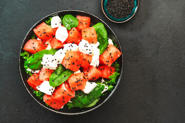 Watermelon salad bowl with feta cheese, spinach and black sesame seed, dark background, top view, copy space