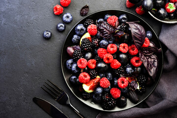 Autumn blue and black berries fruit vegan salad: blueberries, blackberries, grapes, figs and purple basil with honey dressing on dark background, top view